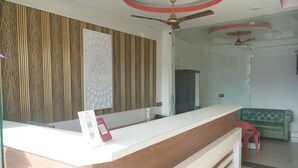 A reception desk with a modern design, a ceiling fan, and a green sofa in the background. - Hotel Aaradhya (Guwahati)