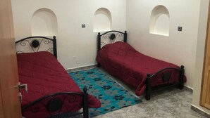 Una habitación pequeña y limpia con dos camas individuales, un tapete azul estampado y paredes blancas con nichos abovedados.