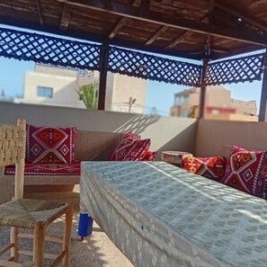 A covered outdoor seating area with a sofa and chair, a patterned cushion, and a blue object on the floor.