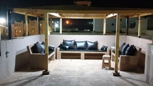 Un espacio al aire libre con piso de piedra, un banco acolchado y una estructura de pérgola de madera.