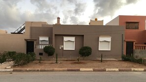 Un edificio residencial con techo plano, un pequeño jardín delantero y una calle al frente.