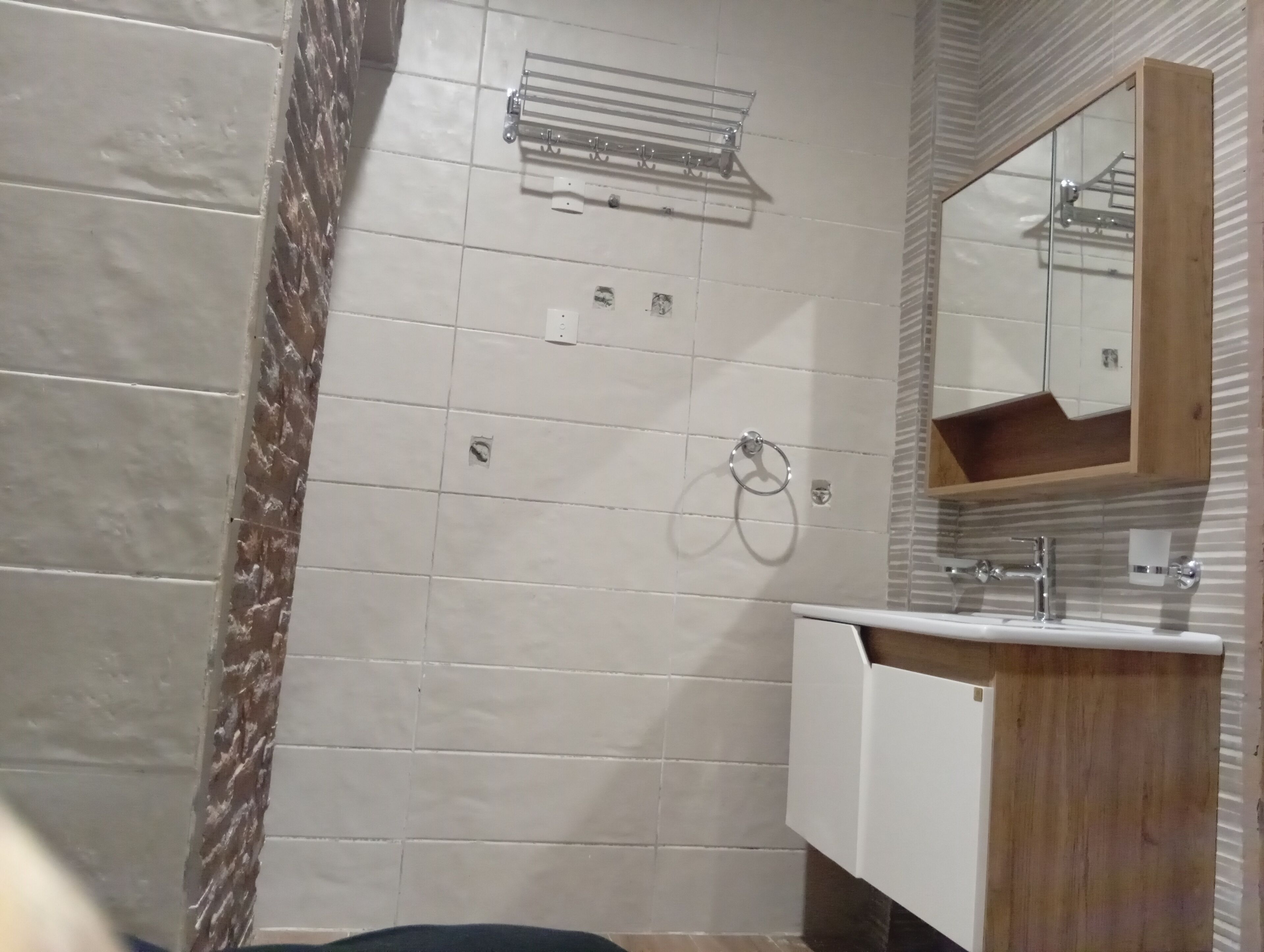 Un bany amb paret de rajola, un suport de tovalloles, un lavabo amb calaixera de fusta i un mirall.