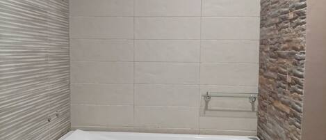 Un baño moderno con una bañera rectangular, paredes con azulejos y un mueble de tocador de madera.