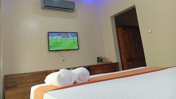 Una habitación de hotel con una cama, un televisor montado en la pared, un aire acondicionado y una puerta de madera.