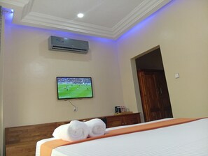Une chambre d’hôtel équipée d’un lit, d’un téléviseur fixé au mur, d’un appareil de climatisation et d’une porte en bois.