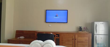 Habitación de hotel con cama, televisor en la pared, escritorio de madera y refrigerador.