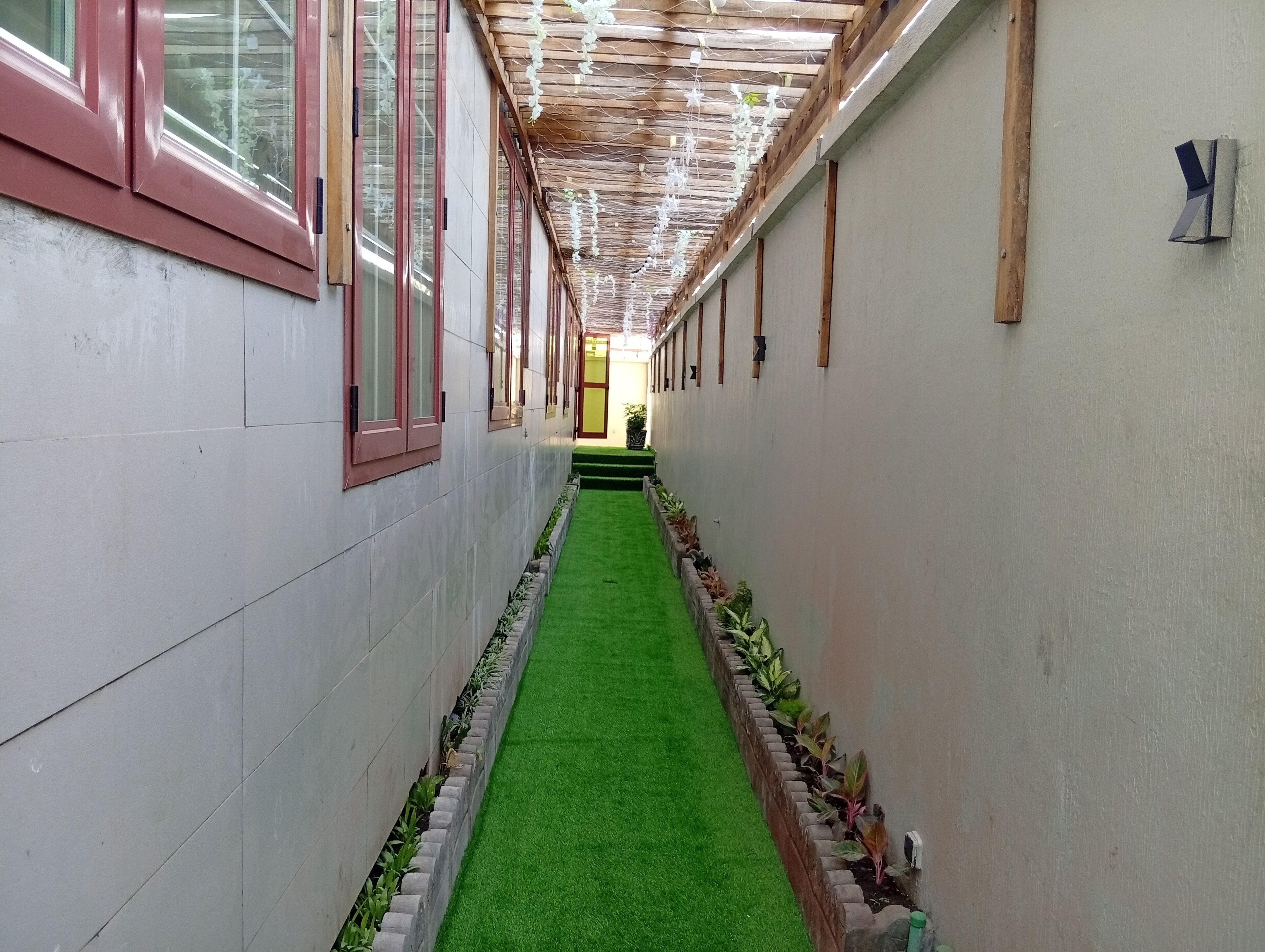 A corridor with a green artificial turf path, tiled walls, and wooden beams on the ceiling.
