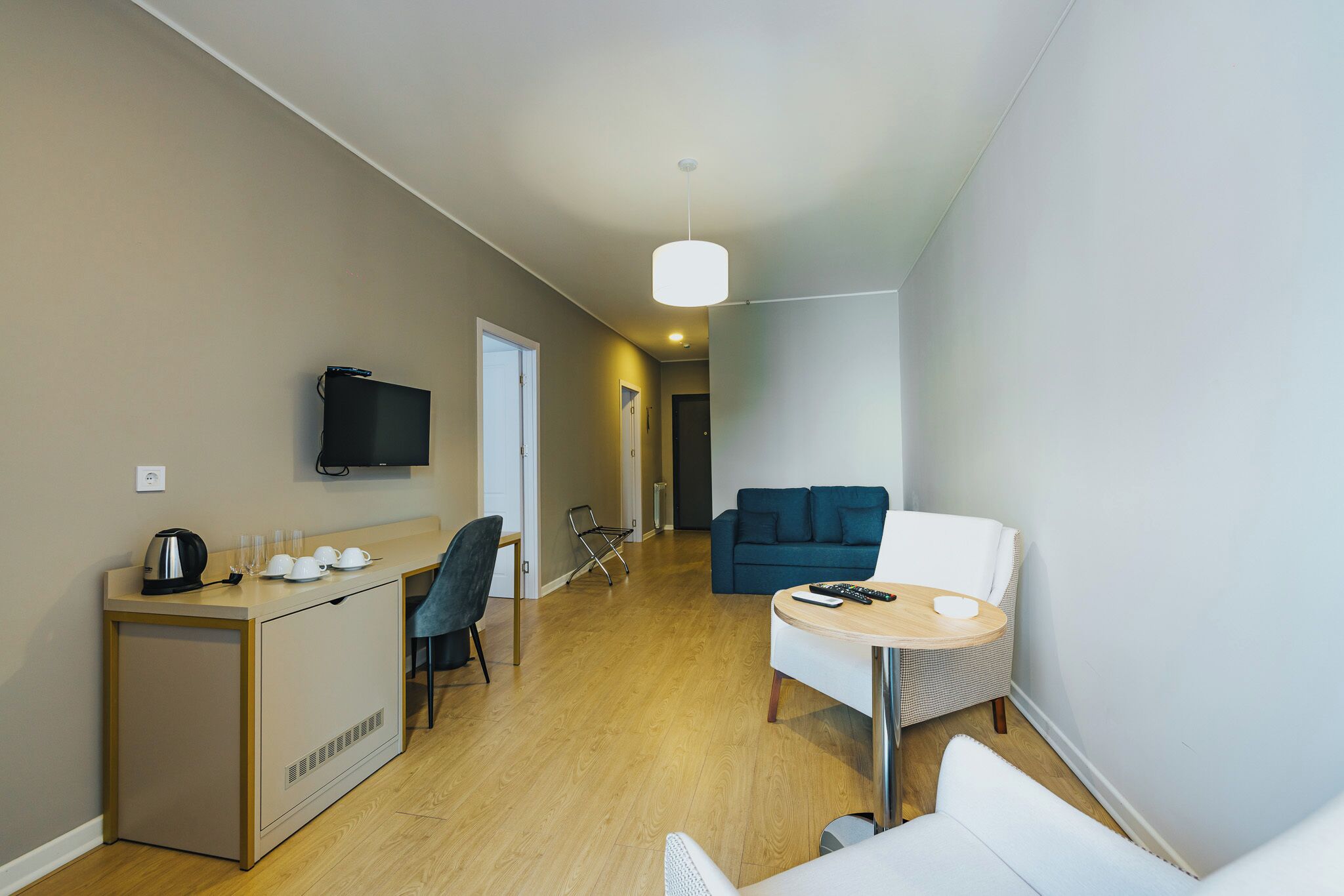 Ett kompakt bostadsutrymme med ett litet kök, en soffa, ett litet bord och en tv som är monterad på väggen.