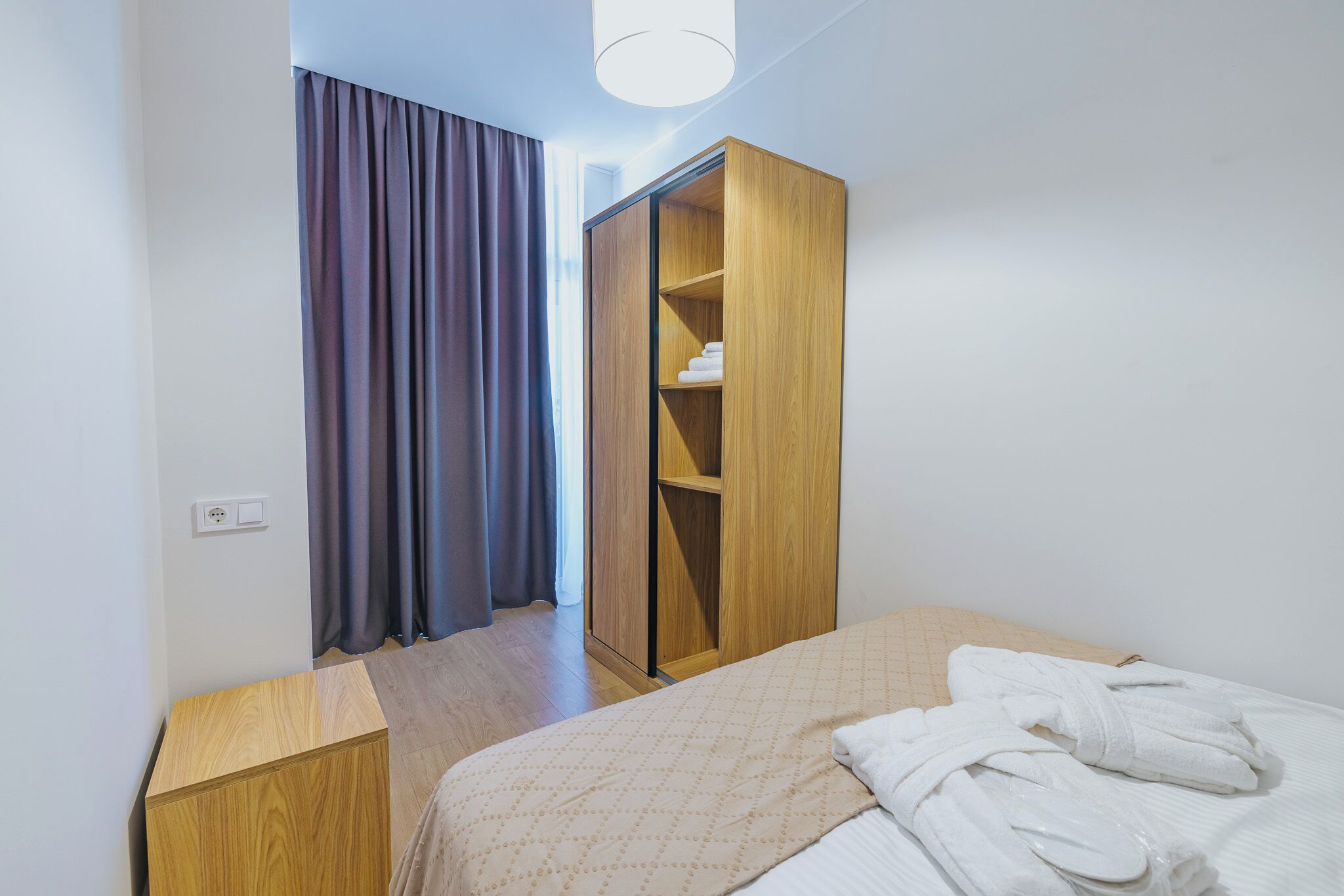 A hotel room with a bed, a wooden wardrobe, and a small wooden nightstand.