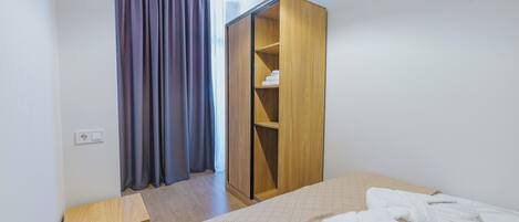 A hotel room with a bed, a wooden wardrobe, and a small wooden nightstand.