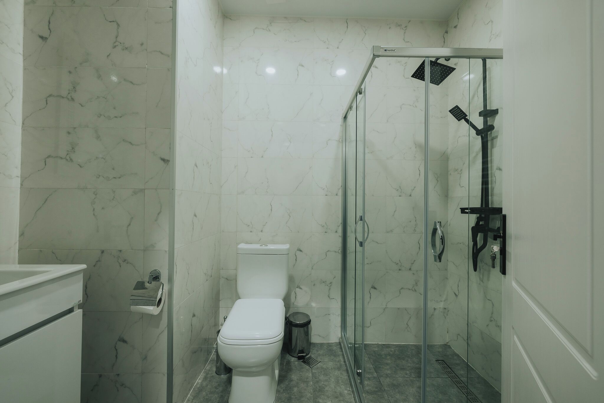 Une salle de bain comprenant des toilettes, une poubelle et une douche séparée par des parois en verre.