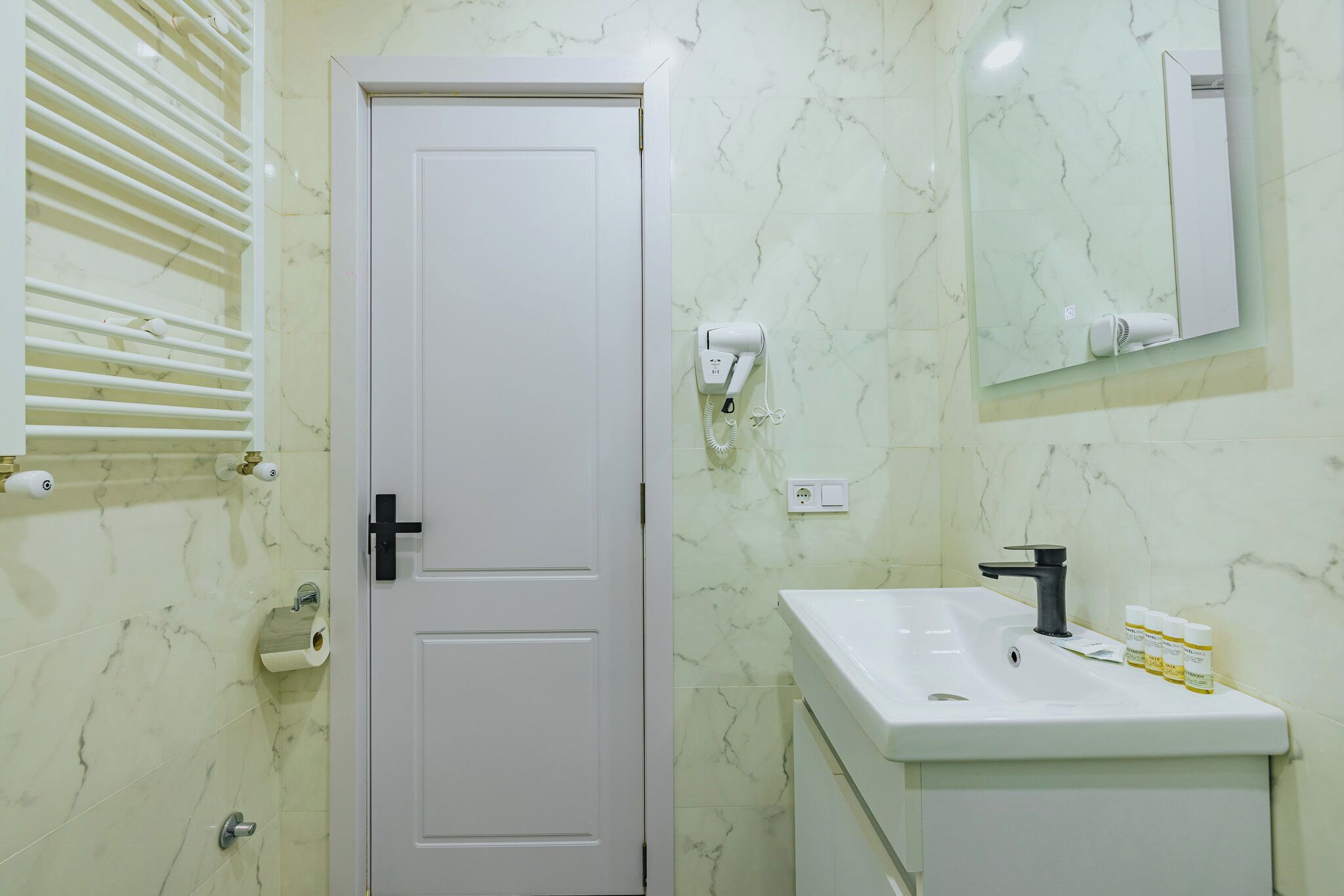 A bathroom with a white door, a sink with a mirror, and a towel rack.