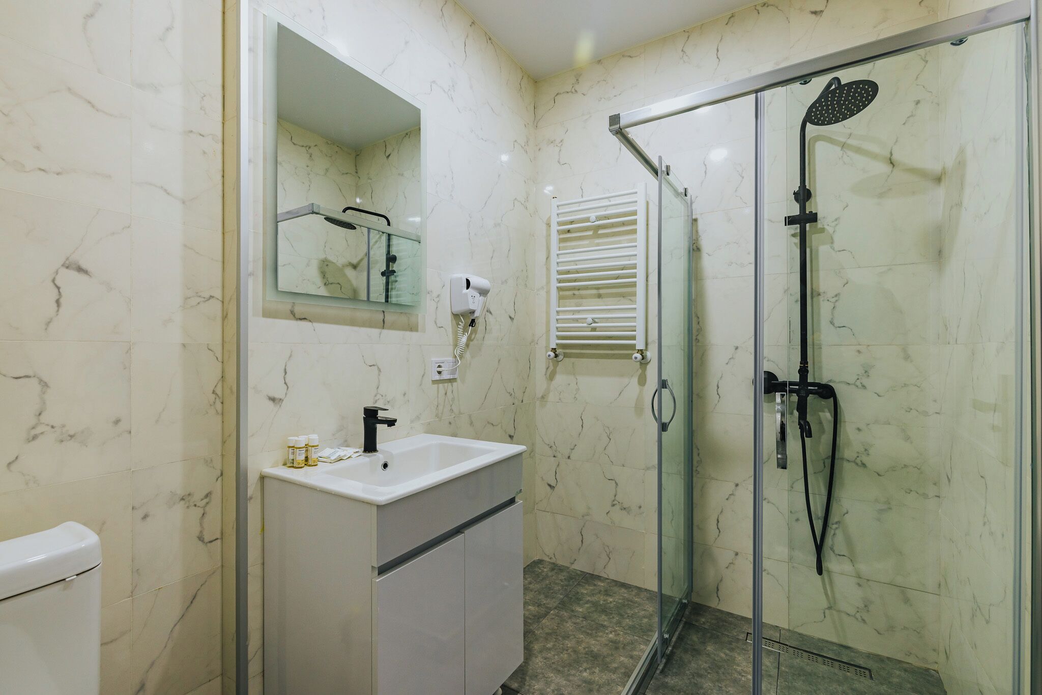 A bathroom with a glass-enclosed shower, a white sink, and a marble-tiled wall.