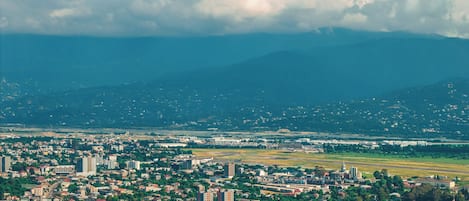 Un paisaje urbano con edificios residenciales y comerciales, un espacio abierto amplio y montañas lejanas bajo un cielo nublado.