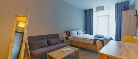 A modern hotel room with a bed, sofa, dining table, and a large mirror.