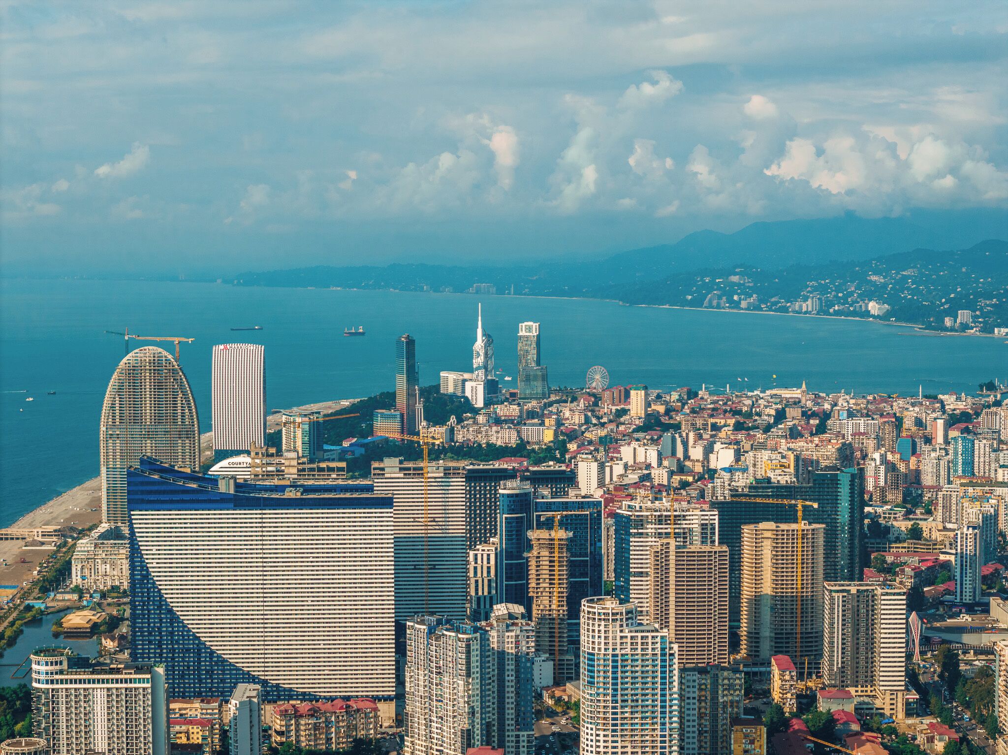 A cityscape with a prominent curved building, several high-rise buildings, and a body of water in the background.