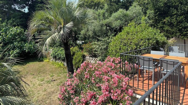 A patio area with a wooden table and chairs, surrounded by lush greenery and flowering plants. - House of 100 m2 on 2 levels with garden of 1000 m2 center Cannes (Cannes)