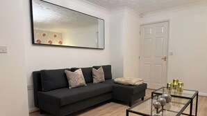 A modern living room with a black sofa, a glass coffee table, and a large mirror on the wall.