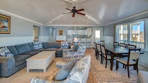 A spacious living room with a large sectional sofa, a dining table with chairs, and a ceiling fan. - Experience Surf City in style at As You Wish! (Surf City)