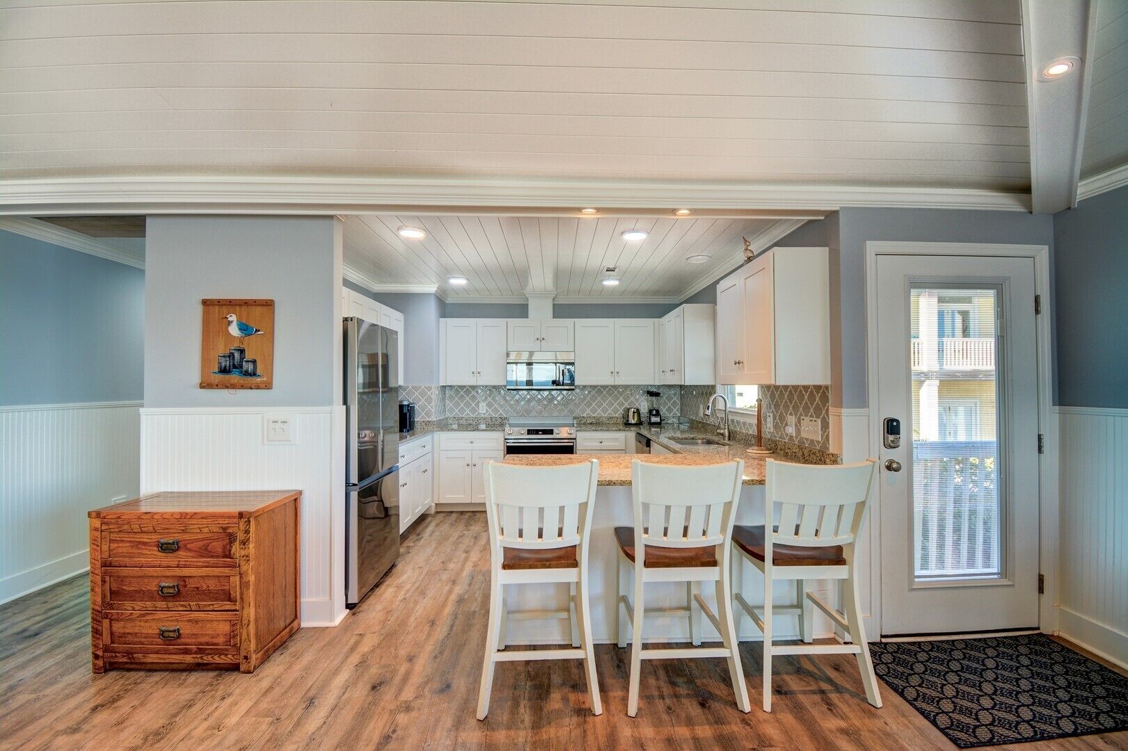 A modern kitchen with white cabinets, a wooden dining table, and three chairs.