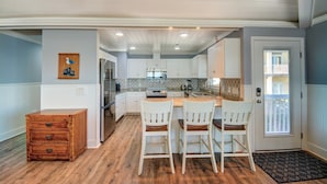 A modern kitchen with white cabinets, a wooden dining table, and three chairs. - Experience Surf City in style at As You Wish! (Surf City)