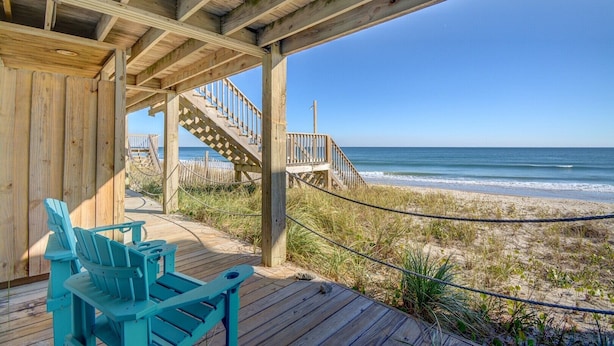 A wooden deck with a view of the beach and ocean, featuring a staircase and two blue Adirondack chairs. - Experience Surf City in style at As You Wish! (Surf City)