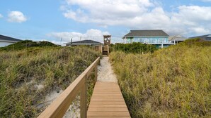 A wooden boardwalk leading to a beach house with a blue exterior, surrounded by dunes and vegetation. - Oceanfront 5-bedroom Relax-Station in Topsail Beach, perfect for family getaways! (Topsail Beach)