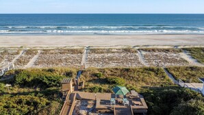An aerial view of a beach resort with wooden walkways, a small building with a green roof, and a sandy beach area. - Oceanfront 5-bedroom Relax-Station in Topsail Beach, perfect for family getaways! (Topsail Beach)