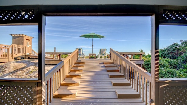 A wooden deck leading to a beach area with a green umbrella, wooden structures, and a clear sky. - Oceanfront 5-bedroom Relax-Station in Topsail Beach, perfect for family getaways! (Topsail Beach)