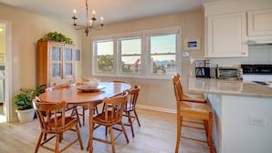 A kitchen with a round wooden table, white cabinets, and a view through large windows. - Oceanfront 5-bedroom Relax-Station in Topsail Beach, perfect for family getaways! (Topsail Beach)