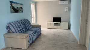 A living room with a sofa, a TV on a white cabinet, and a painting on the wall.