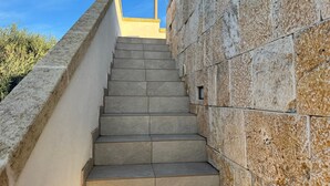 A staircase leading upwards, flanked by stone walls, with a clear blue sky in the background.