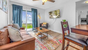 Een woonkamer met een bank, salontafel en eettafel, een plafondventilator en een televisie aan de muur.