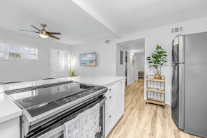 Une cuisine moderne dotée d’une cuisinière intégrée, de meubles blancs, d’un ventilateur de plafond et d’un réfrigérateur en acier inoxydable.