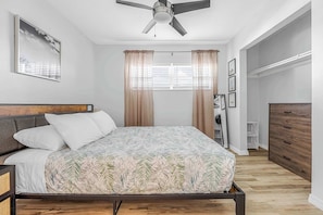 Une chambre à coucher avec un lit, des rideaux, un ventilateur de plafond, une fenêtre et une armoire en bois.