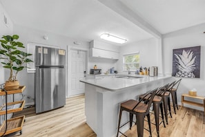 A modern kitchen with a stainless steel refrigerator, a central island with bar stools, a microwave, and a sink.
