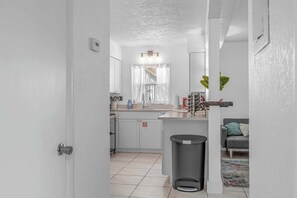 Une cuisine équipée d’un évier, d’une poubelle et d’une fenêtre avec un rideau.