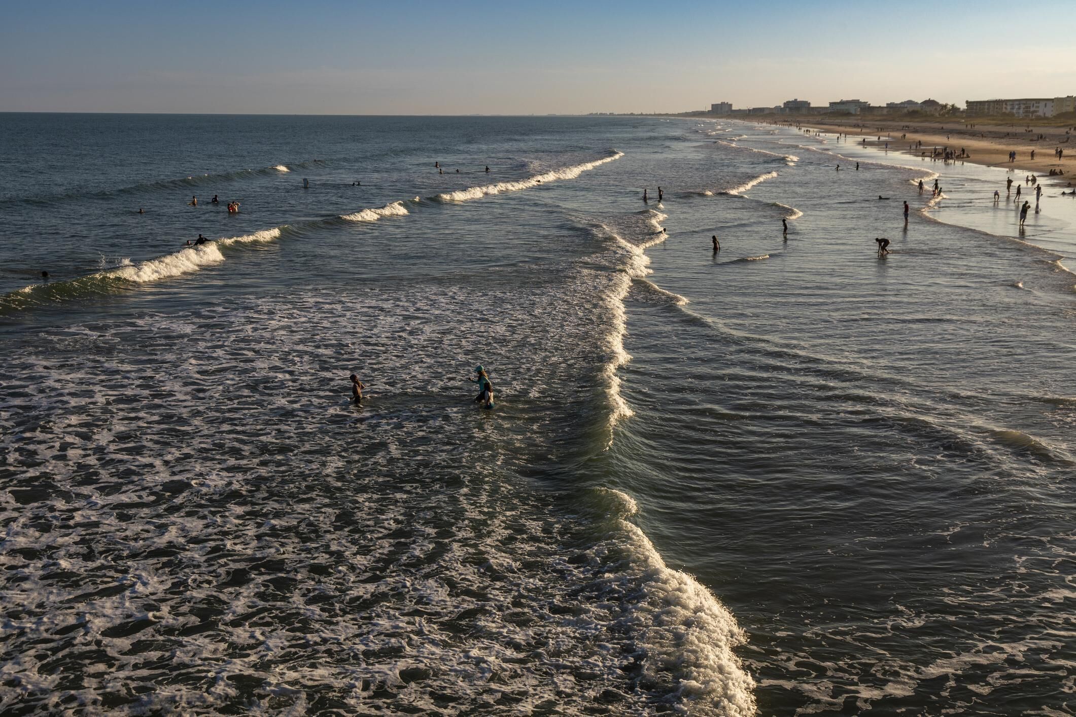 A beach with waves, people, and a distant shoreline.