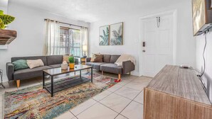 A modern living room with a sofa, coffee table, and a rug. - Walk to Beach - 2BR Between River & Ocean (Cocoa Beach)