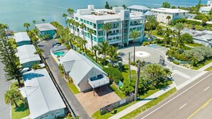 An aerial view of a coastal hotel with multiple buildings, a swimming pool, and a road with a clear view of the ocean. - Walk to Beach - 2BR Between River & Ocean (Cocoa Beach)