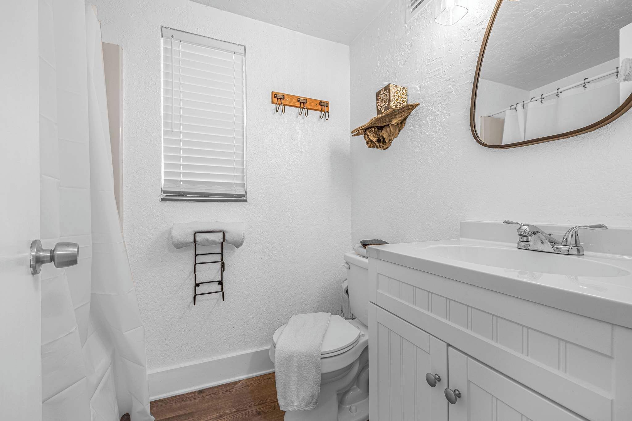 A bathroom with a toilet, sink, mirror, towel rack, and a window with blinds.