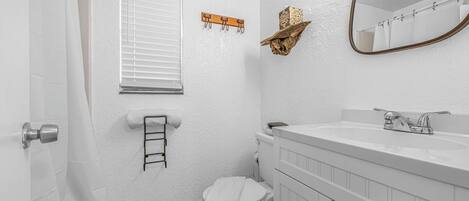 A bathroom with a toilet, sink, mirror, towel rack, and a window with blinds.