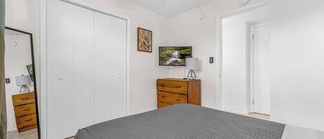 Ein Schlafzimmer mit Bett, Deckenventilator, Fernseher, Kommode und einer Tür.