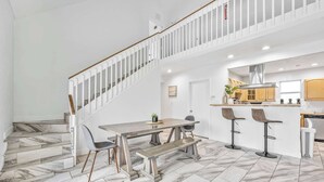 Uma cozinha ampla com design moderno, uma área de refeições com mesa e banco de madeira, e uma escada com guarda-corrimão branco.
