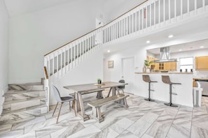 Une cuisine spacieuse au design moderne, un coin repas avec une table et un banc en bois, et un escalier avec des rampes blanches.
