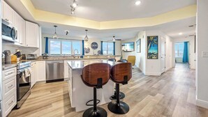 A modern kitchen with white cabinets, a stainless steel dishwasher, and a wooden island with two bar stools. - RIVER FLY IN: Updated, Luxurious Waterfront 2BR (Merritt Island)
