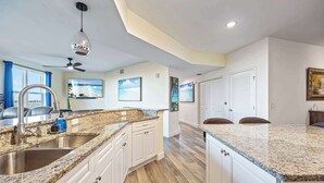 A kitchen with granite countertops, white cabinets, a stainless steel sink, a ceiling fan, and a pendant light. - RIVER FLY IN: Updated, Luxurious Waterfront 2BR (Merritt Island)