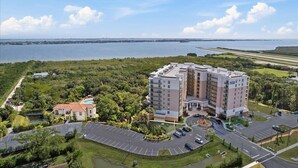 A multi-story hotel with a pool, surrounded by greenery and a body of water. - RIVER FLY IN: Updated, Luxurious Waterfront 2BR (Merritt Island)