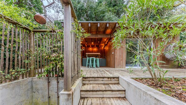 Una escalera de madera que lleva a un espacio al aire libre techado con una mesa y sillas.