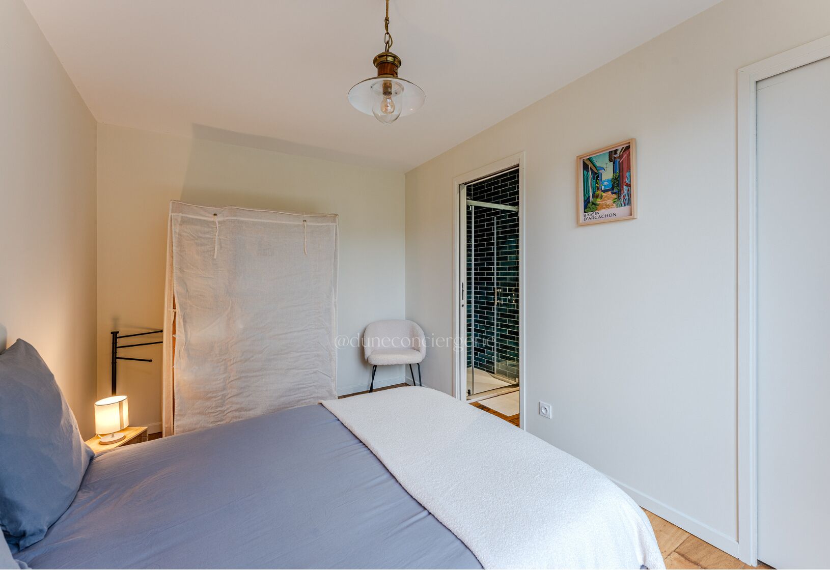 A bedroom with a bed, a chair, a lamp, a door, and a painting on the wall.